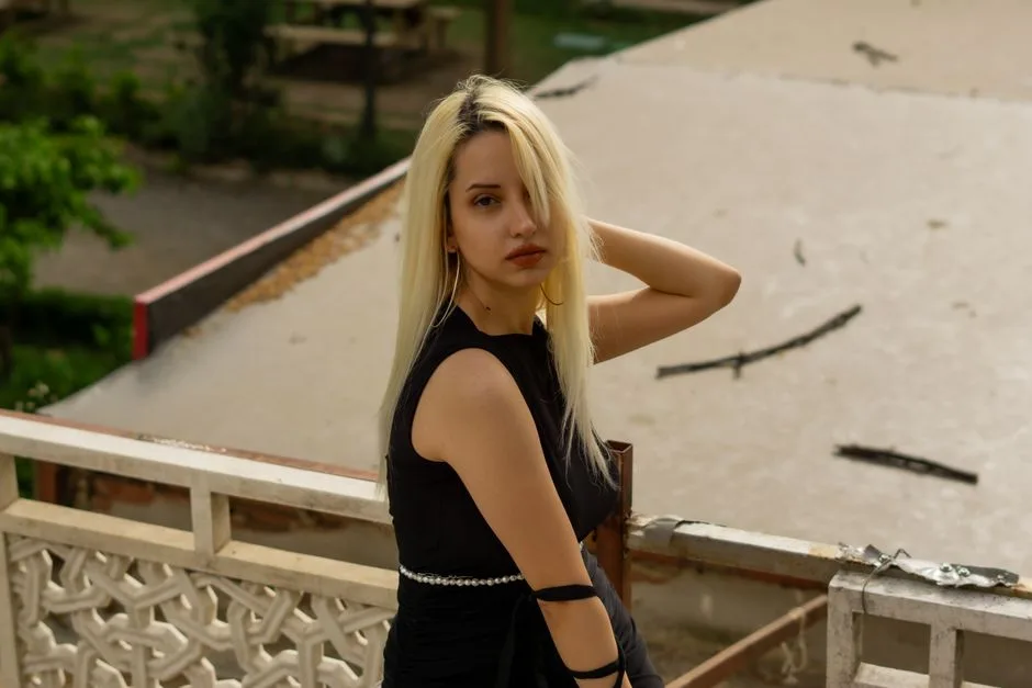 Blonde woman posing on a balcony in an urban outdoor setting during the day.
