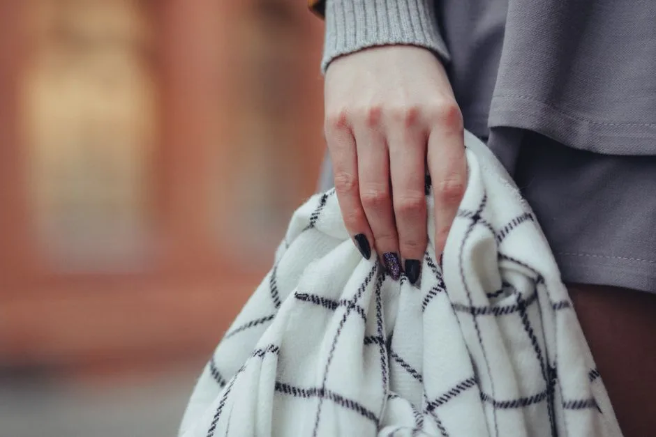 A woman's hand with intricate nail art holding a patterned blanket in a stylish close-up shot.