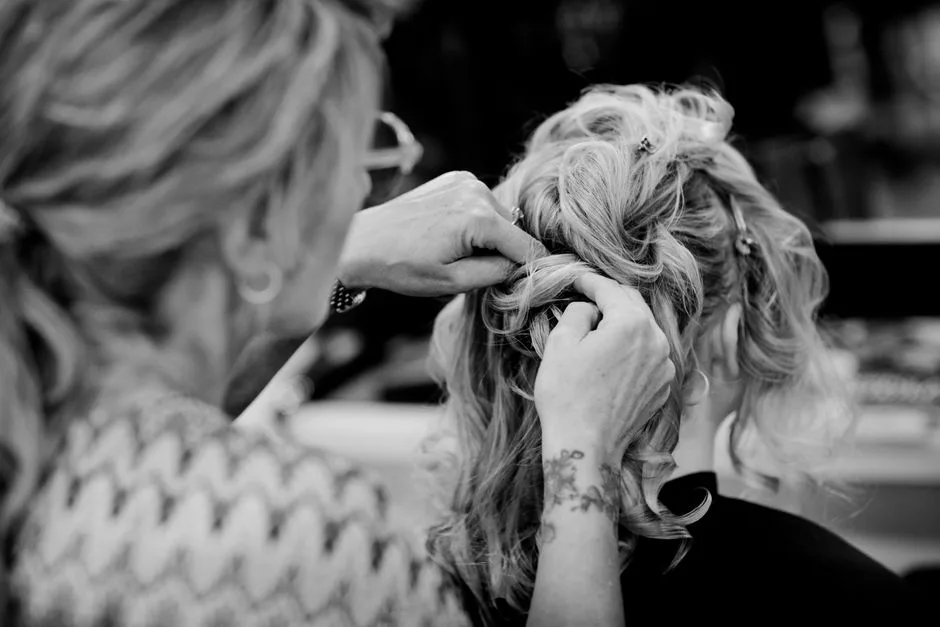 Black and white photo of a hairstylist crafting an elegant updo on a woman's hair.
