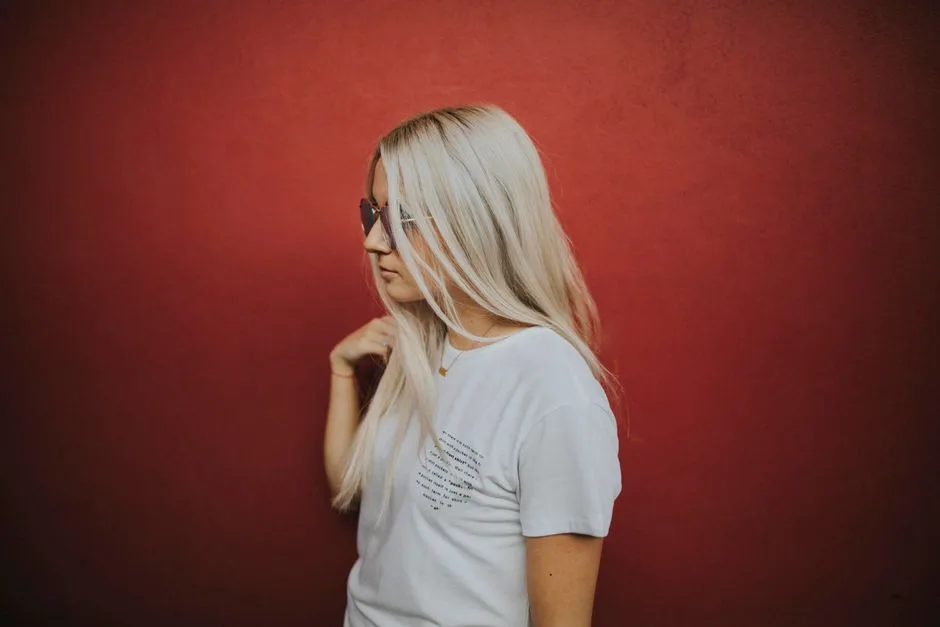 Side view of a blonde woman wearing sunglasses, standing against a red wall.