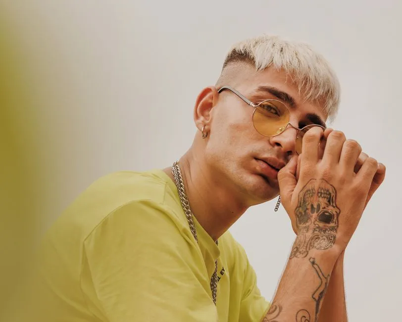 Trendy portrait of a young man with blonde hair, tattoos, and stylish eyewear.