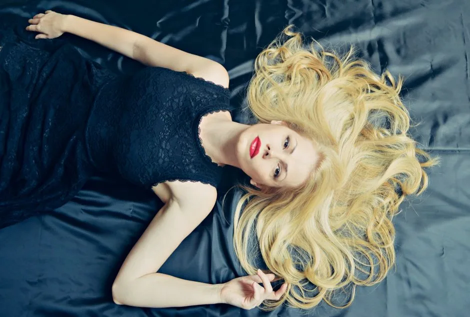 Elegant fashion portrait of a blonde woman in a luxurious black dress, lying gracefully.
