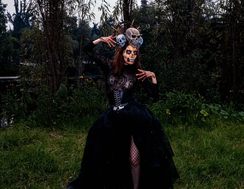A person in gothic costume and skeleton makeup in a dark outdoor setting, evoking Halloween vibes.