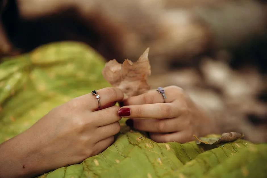 Hands adorned with rings gently holding an autumn leaf.