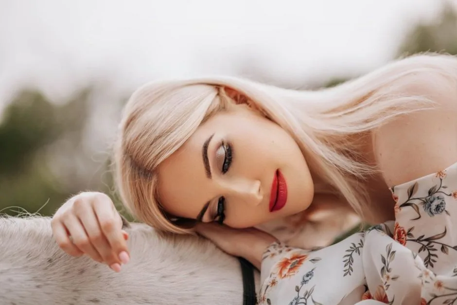 Blonde woman in floral dress rests outdoors, serene and relaxed.