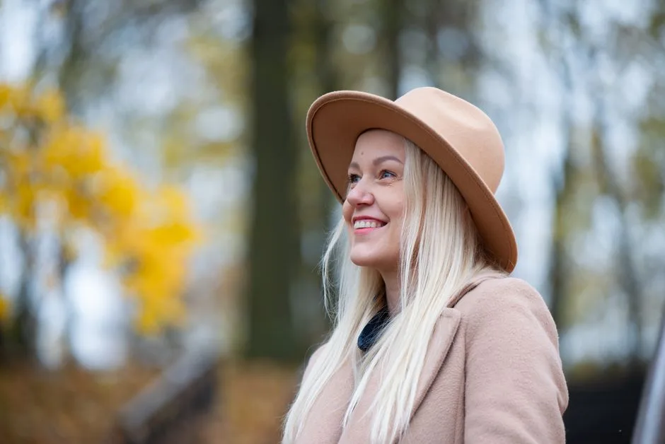 Blonde woman smiling outdoors in fall wearing a beige hat and coat.