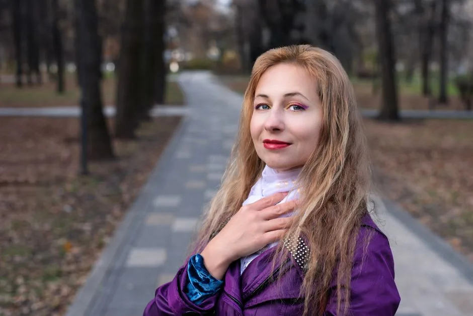 Young woman in a purple coat strolling through a park during fall. Bright makeup and confident smile.