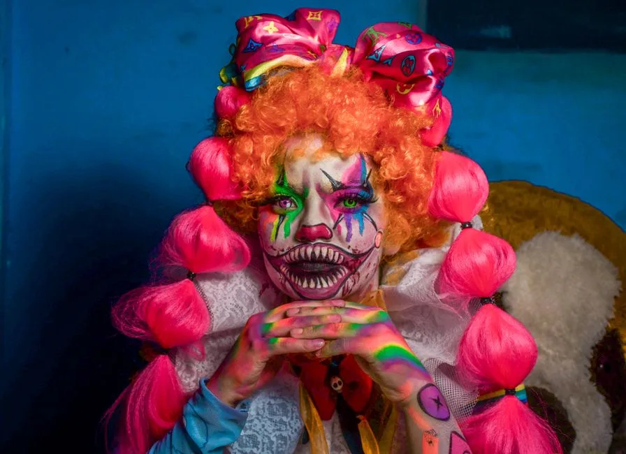 Vibrant clown portrait with vivid makeup and colorful hair indoors.