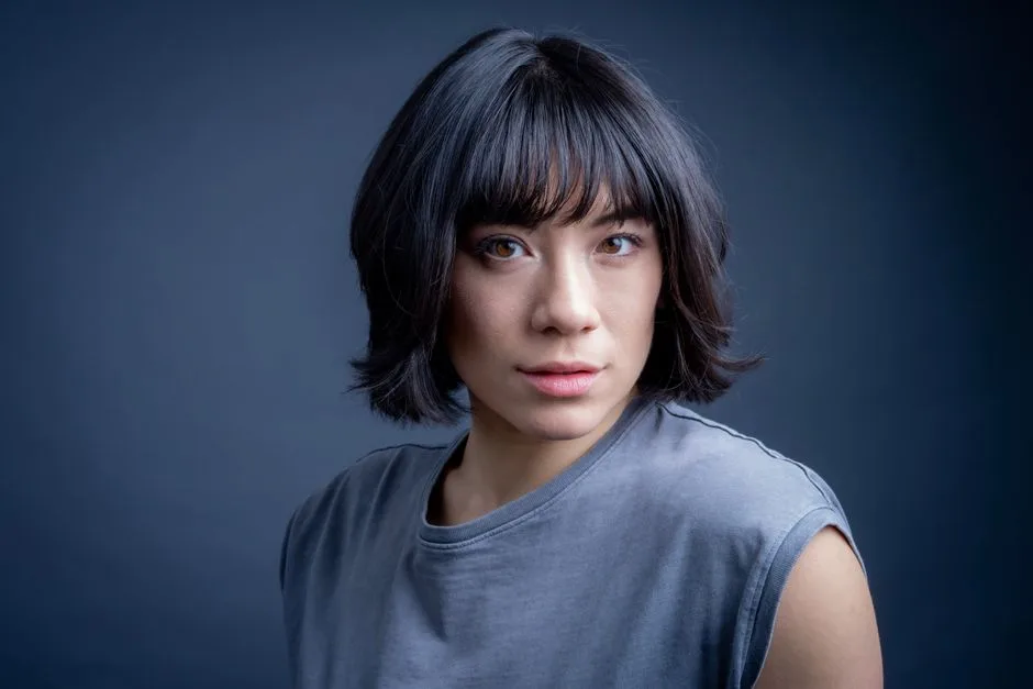 Studio portrait of a woman with dark short hair and a neutral expression in soft lighting.