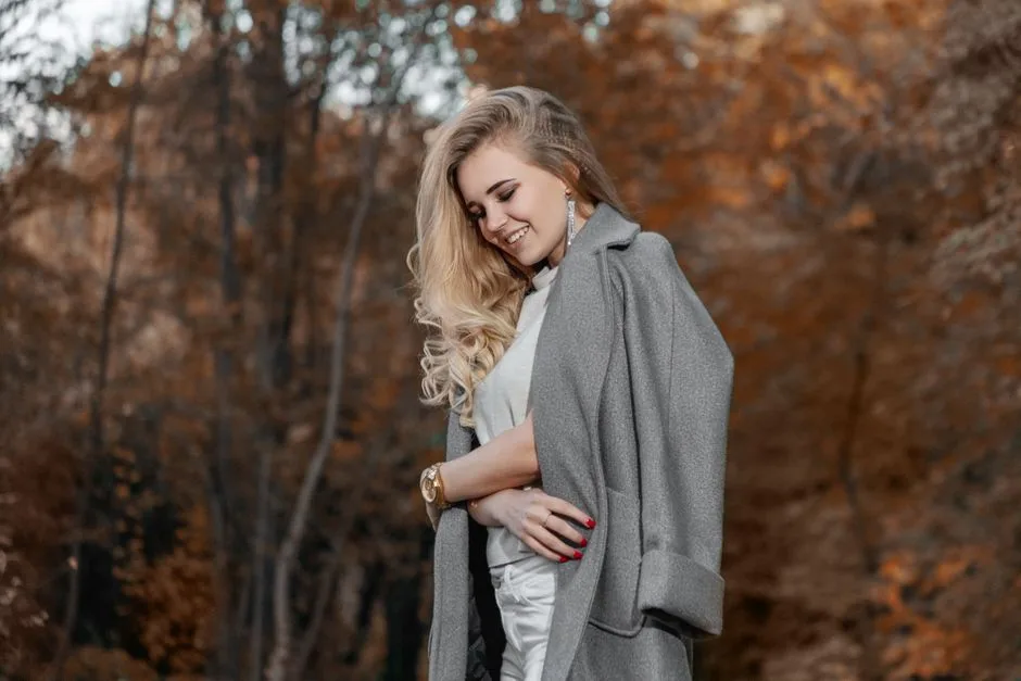 Blonde woman with a fashionable coat enjoying a serene autumn day outdoors.