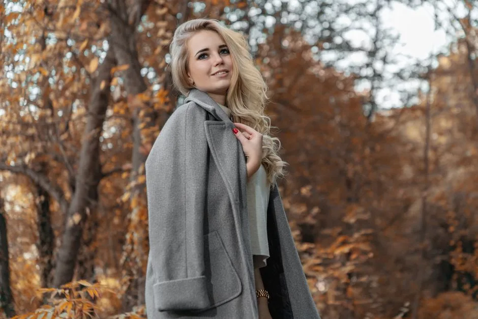 Side view charming female with curly hair wearing gray coat amidst trees with yellow leaves in autumn park