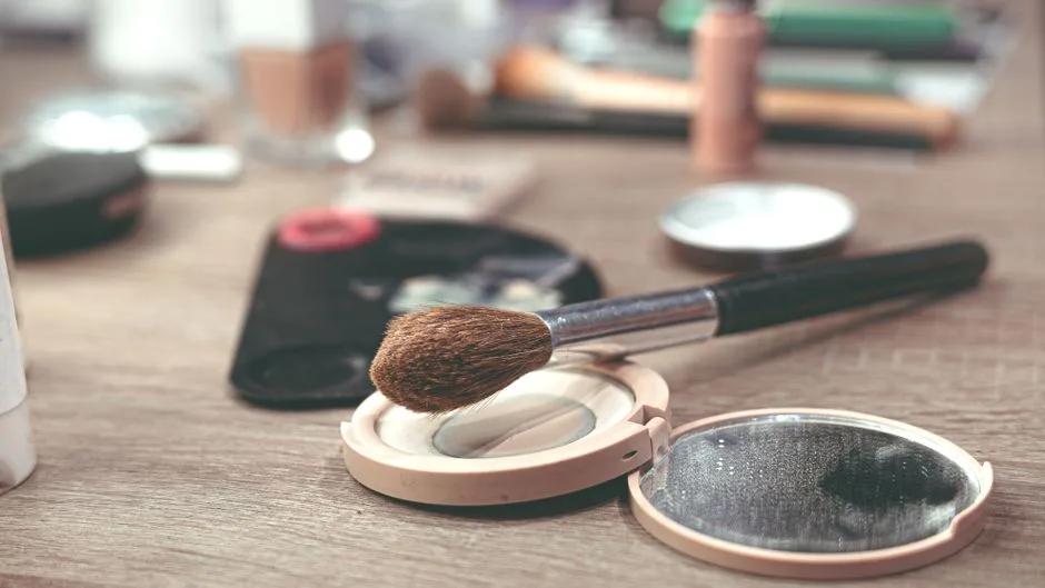 Close-up image of makeup brushes and compact powder on a wooden surface, ideal for beauty themes.