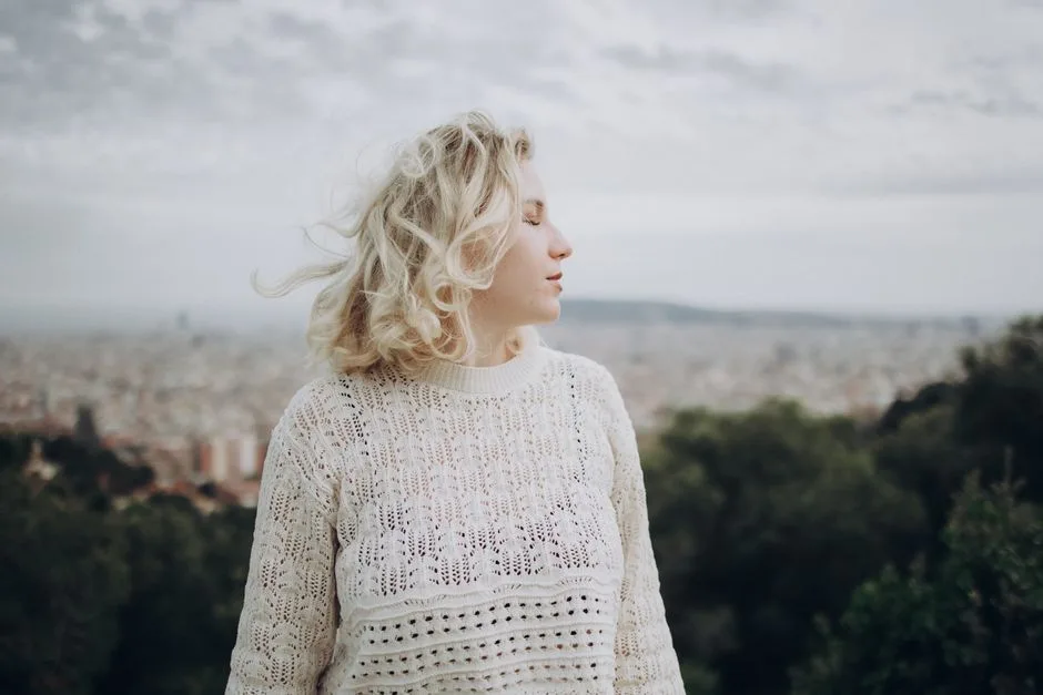 A woman in a white knit sweater gazes over a scenic city view, capturing a serene outdoor moment.