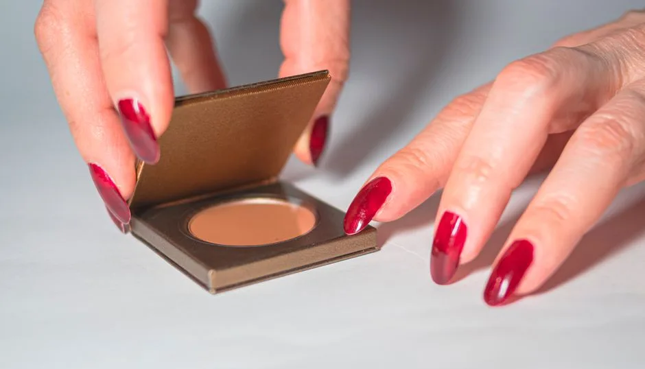 Close-up of female hands with red nails opening a makeup compact.