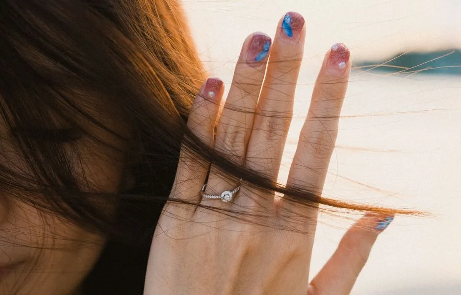A hand with colorful nail art and a sparkling ring is captured against a soft background.