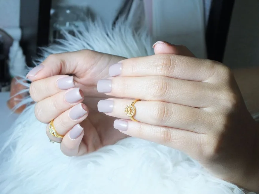 Close-up of beautiful manicured hands showcasing grey nails and gold rings in a serene setting.