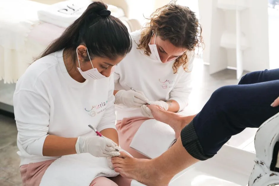 Two technicians performing detailed pedicure on client in modern nail salon.