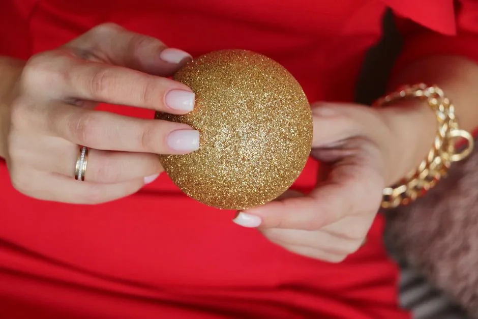 Hands holding a glittery gold ornament on a red background, festive and elegant.