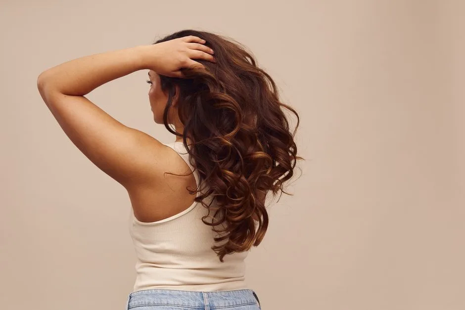 Elegant back view of a woman with long, curly brown hair in a stylish pose.