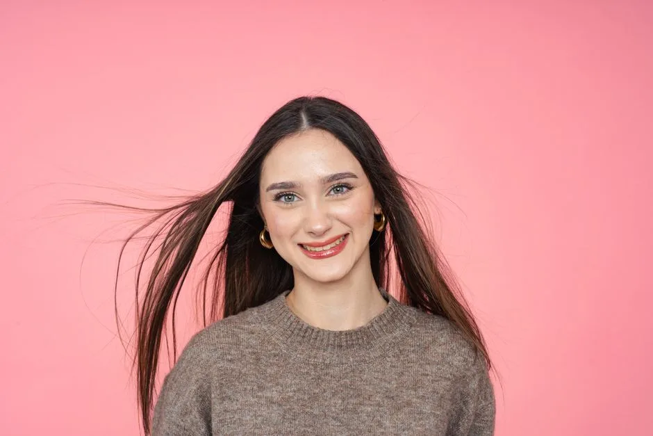 Smiling woman with flowing hair against pink background, wearing a sweater.