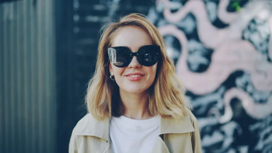 Portrait of a fashionable woman wearing sunglasses, smiling outdoors.