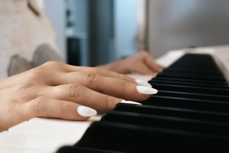 A close-up view of a female adult's hands playing a piano indoors, focusing on fingering technique and white nails.