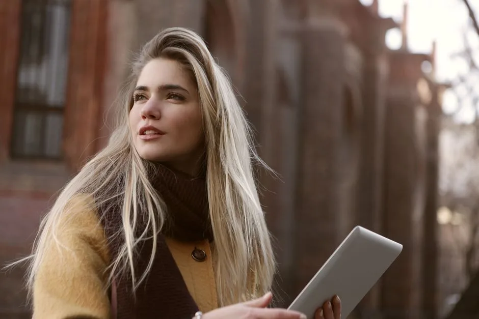 Young woman with long blonde hair holding a tablet outside. Enjoying the view.
