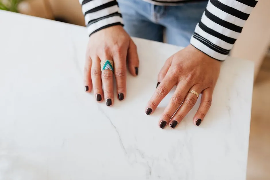 From above unrecognizable woman demonstrating hands with manicured nails on white table in apartment during weekend