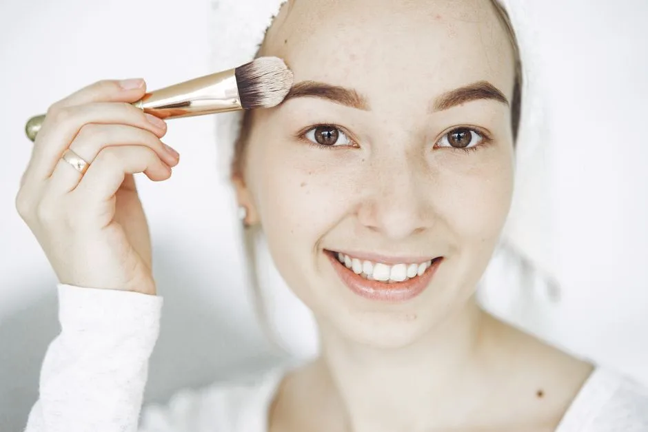 Portrait of a smiling young woman applying makeup with a brush indoors.