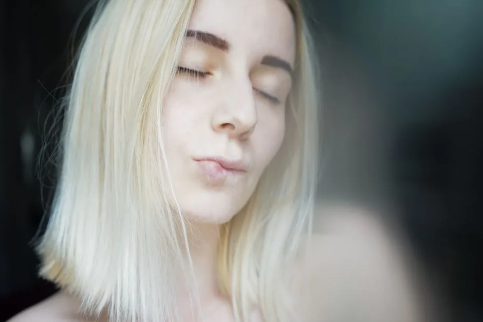 Crop pretty young woman with blond hair and dark eyebrows delicately pursing lips