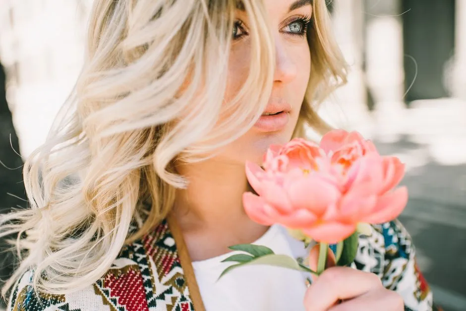 Close-up of a blonde woman holding a pink flower, showcasing beauty and nature.