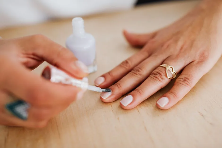 Detailed view of a hand receiving a manicure with nail polish application and a gold heart ring.