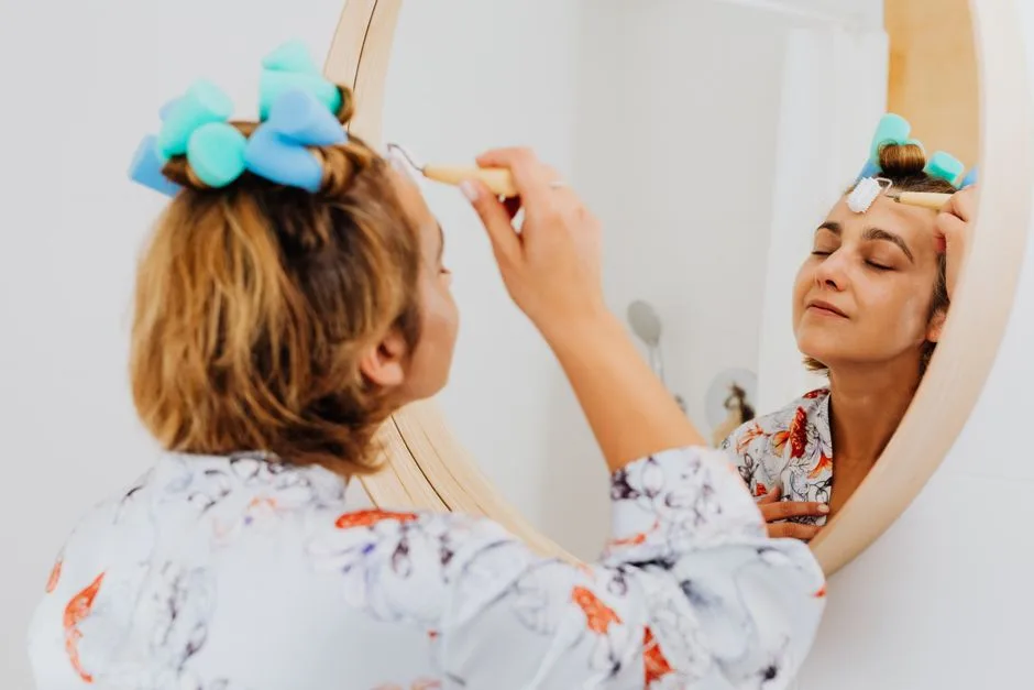 Woman with closed eyes applying skincare product in front of mirror, enjoying self-care time.