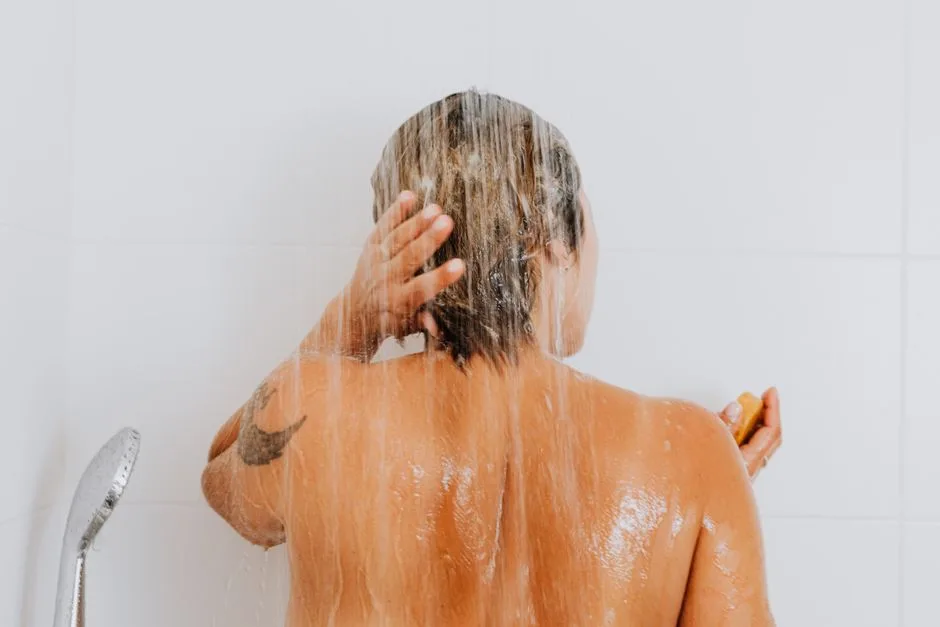 Rear view of a woman rinsing hair under shower, capturing an intimate and refreshing moment indoors.