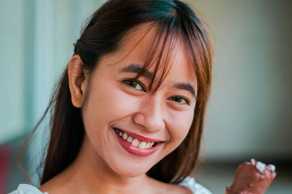 Headshot of cheerful Asian female with brown hair smiling and looking at camera while standing with chocolate ice cream on blurred background
