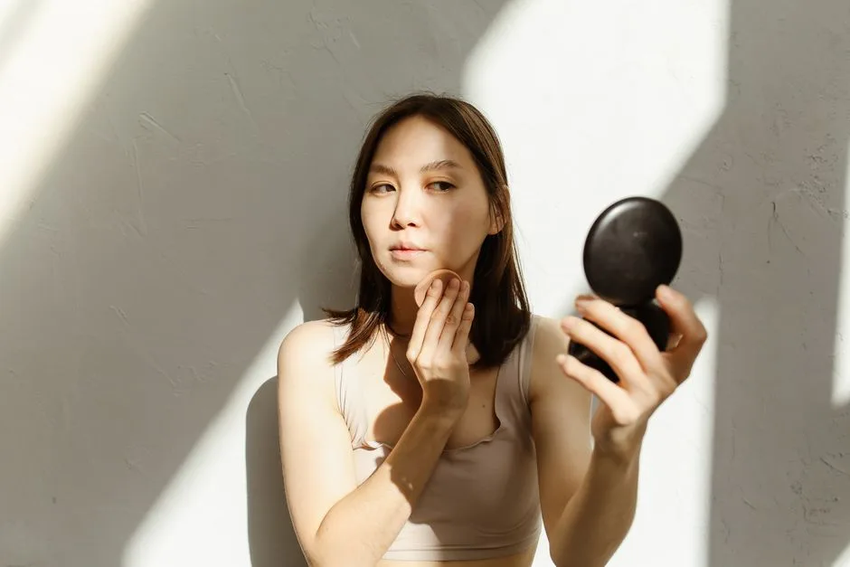 A young woman applying makeup, illuminated by natural light streaming through a window.