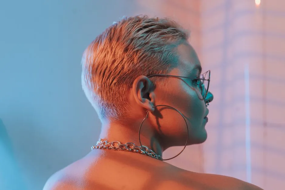 Close-up profile of a stylish woman with blonde short hair, hoop earrings, and chain necklace in vibrant lighting.