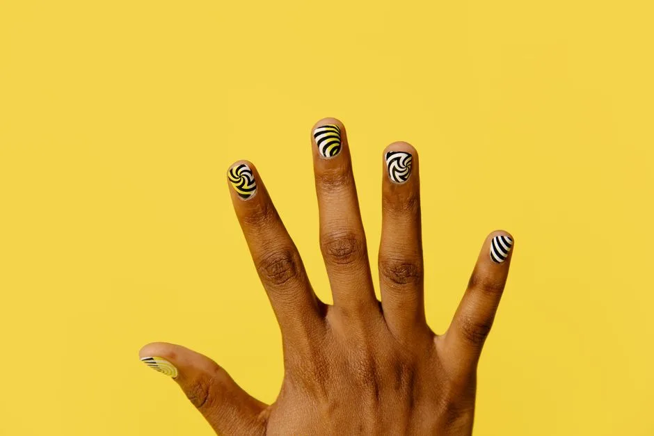 Close-up of a hand with vibrant patterned nail art against a bright yellow background.