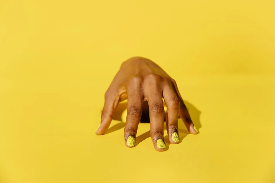 Stylish yellow nail art on a hand against a vibrant yellow background, perfect for beauty and fashion themes.