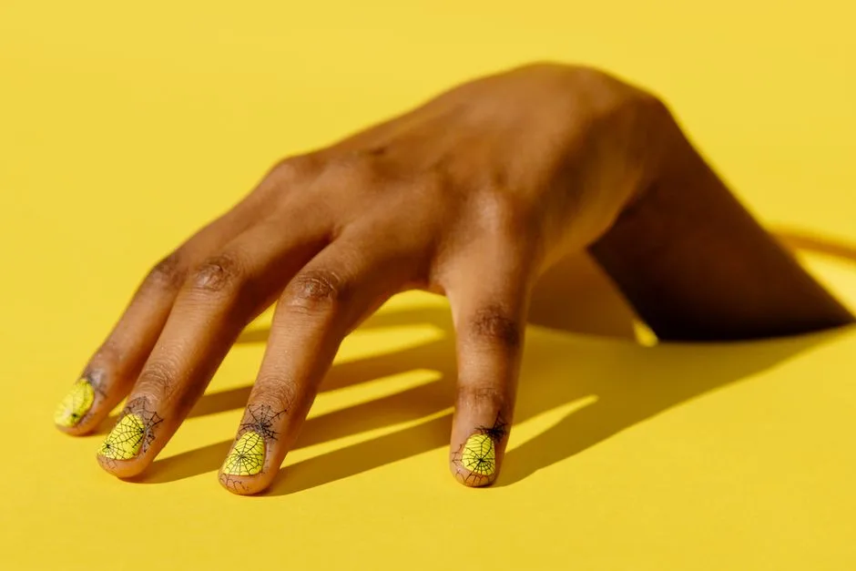 Close-up of a hand showcasing yellow nail art with intricate designs on a vibrant background.