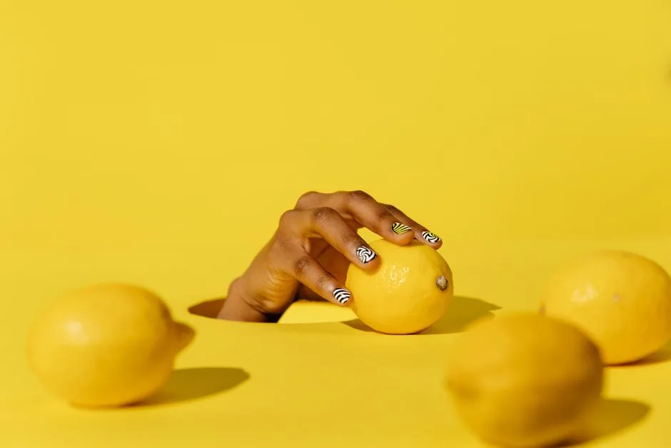 Striking yellow lemons held by a hand with stylish nail art, set against a vibrant lemon-colored backdrop.