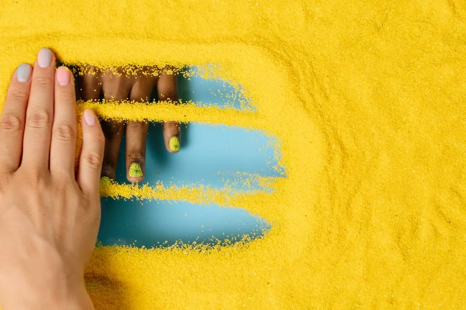 Creative composition of hands with colorful nails in vibrant yellow sand. Perfect for fashion or art concepts.