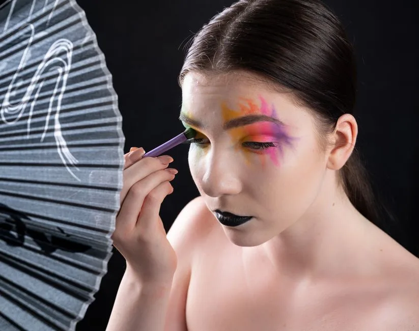 Close-up of a woman applying vibrant eye makeup with an artistic touch.