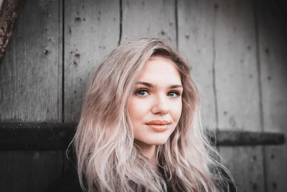 Portrait of a blonde woman with lip piercing against a wooden backdrop.