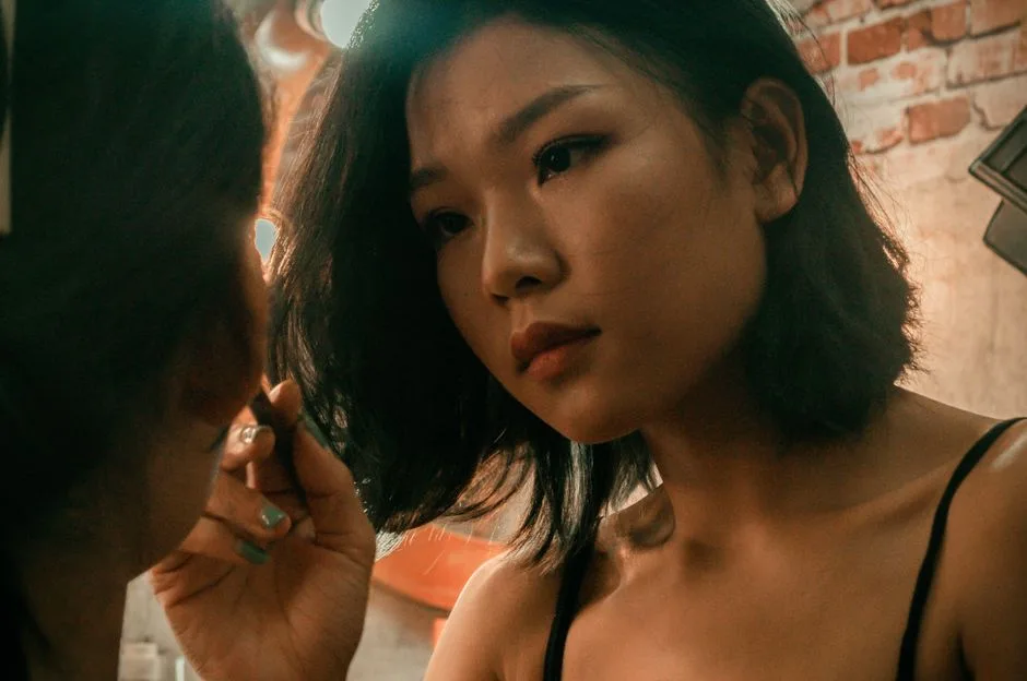 Close-up of a woman applying makeup in an indoor setting with a warm mood.