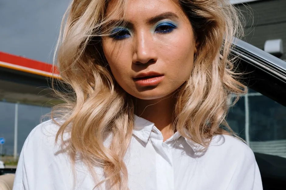 Close-up portrait of a woman with bold blue eyeshadow and blonde hair outdoors.