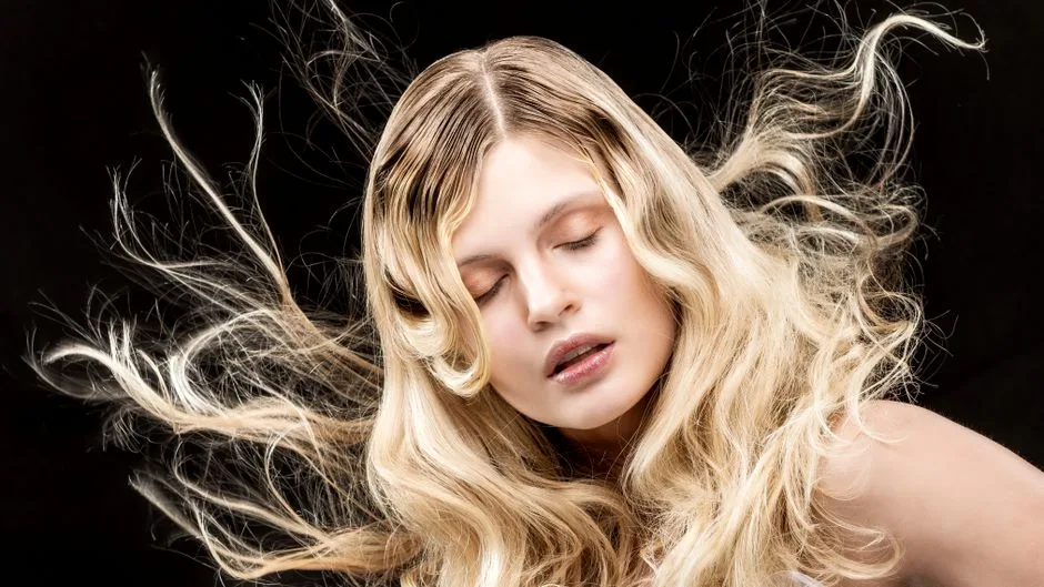Stylish portrait of a woman with flowing blonde hair and closed eyes on a black background.