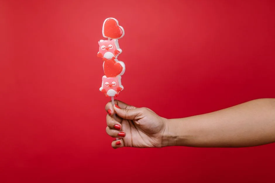 A hand holding a heart-shaped lollipop with a red background, perfect for Valentine's Day.