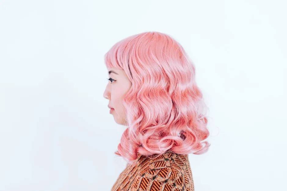 Studio portrait featuring a side view of a woman with striking pink hair and a patterned top.
