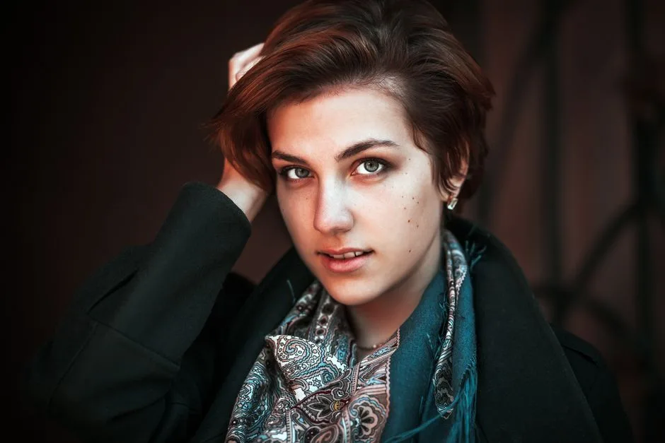 Portrait of a chic short-haired woman in a stylish coat and scarf, posing confidently indoors.